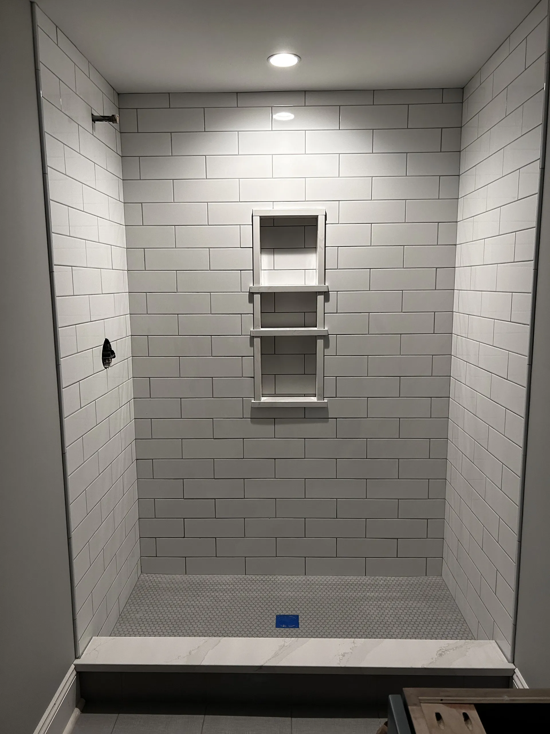 Custom walk-in shower with white subway tile walls and built-in storage niche